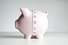 measuring tape around piggy bank, paring down expenses concept