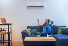 women on a couch turning on her heat pump to regulate the temperature of her home