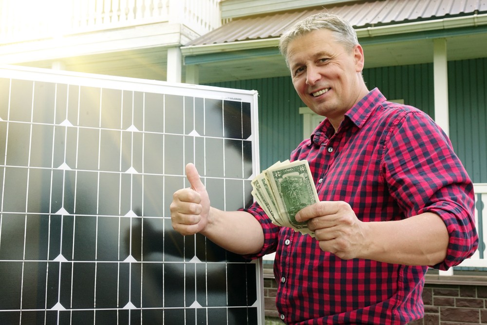 man giving thumbs up holding money next to solar panel