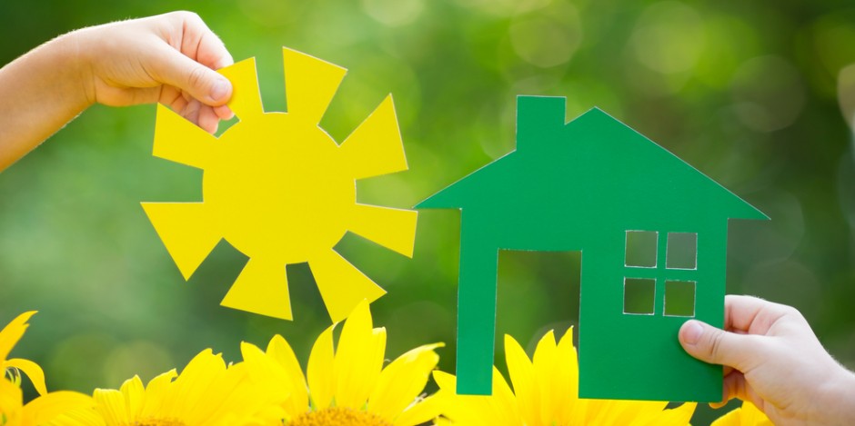 Two hands holding paper house and sun over flowers