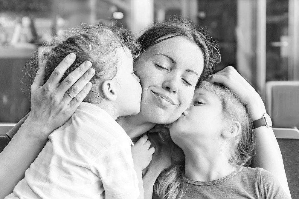 two children kissing and hugging their mother