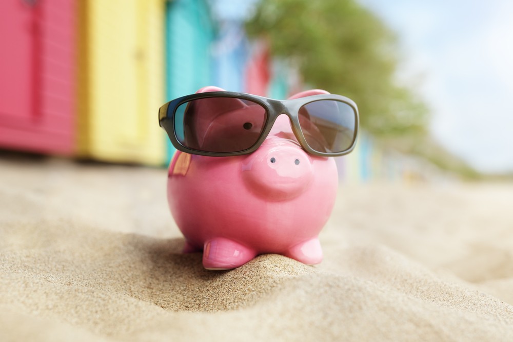 savings piggy bank on a beach with sunglasses, summer savings concept