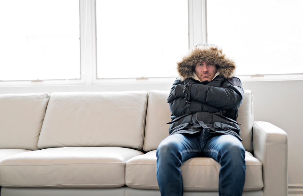 man in a winter coat angrily sitting on a couch